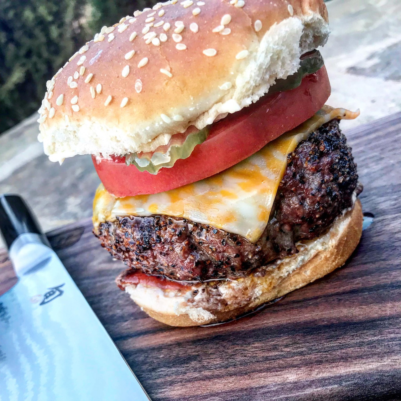 Close-up of a cheeseburger with melted cheese, tomato, and lettuce on a sesame seed bun