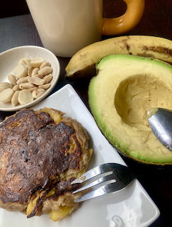 Breakfast plate with a browned pancake, avocado half, banana, mug, and small bowl of seeds