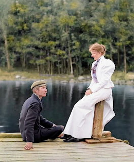 Vintage-dressed man and woman sitting on a wooden dock by a calm lake