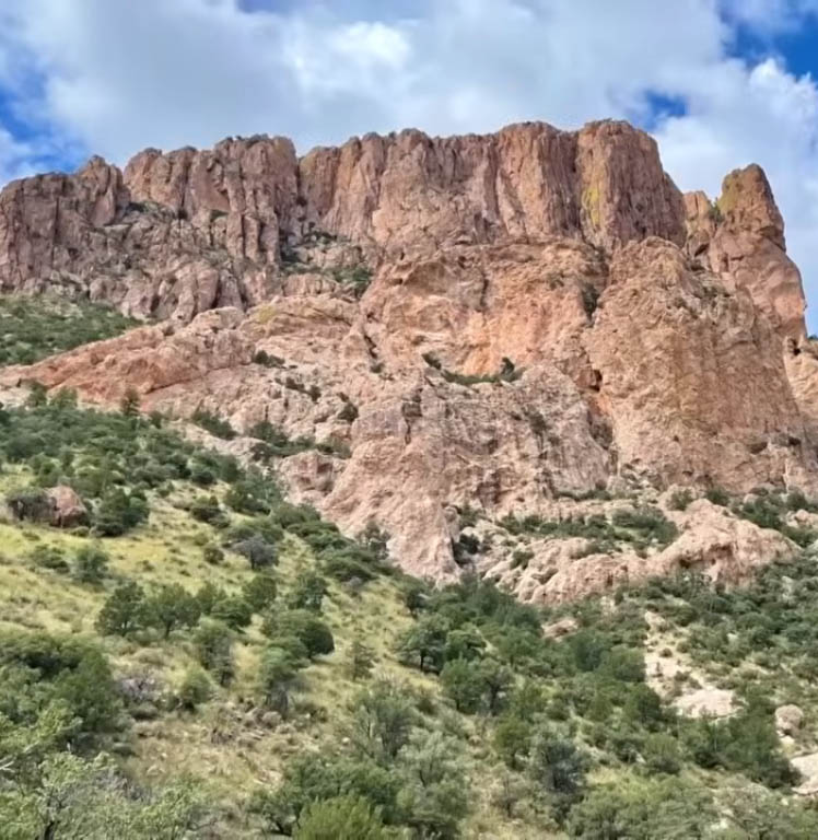 Rocky cliffs above a green hillside under a partly cloudy sky