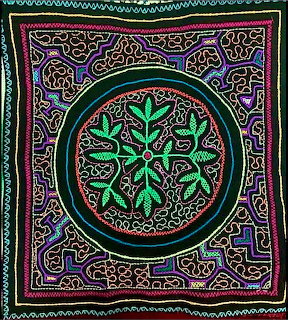Colorful embroidered textile with circular green leaf mandala and geometric patterns on black background