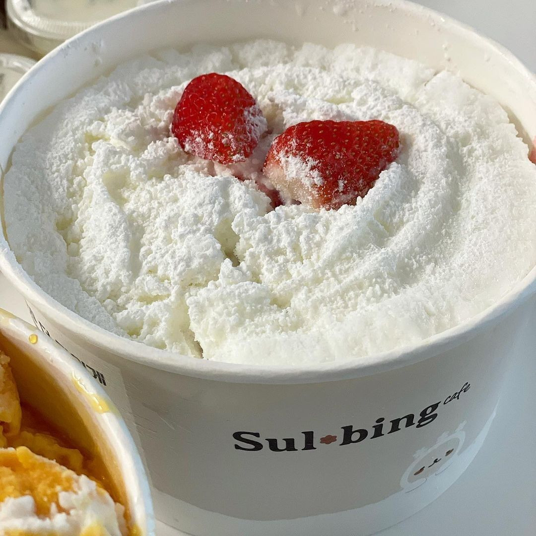 White bowl of milk bingsu topped with strawberries and powdered milk