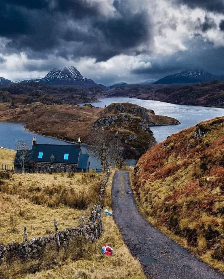 Small cottage on hillside path with mountains and stormy sky in Scottish Highlands