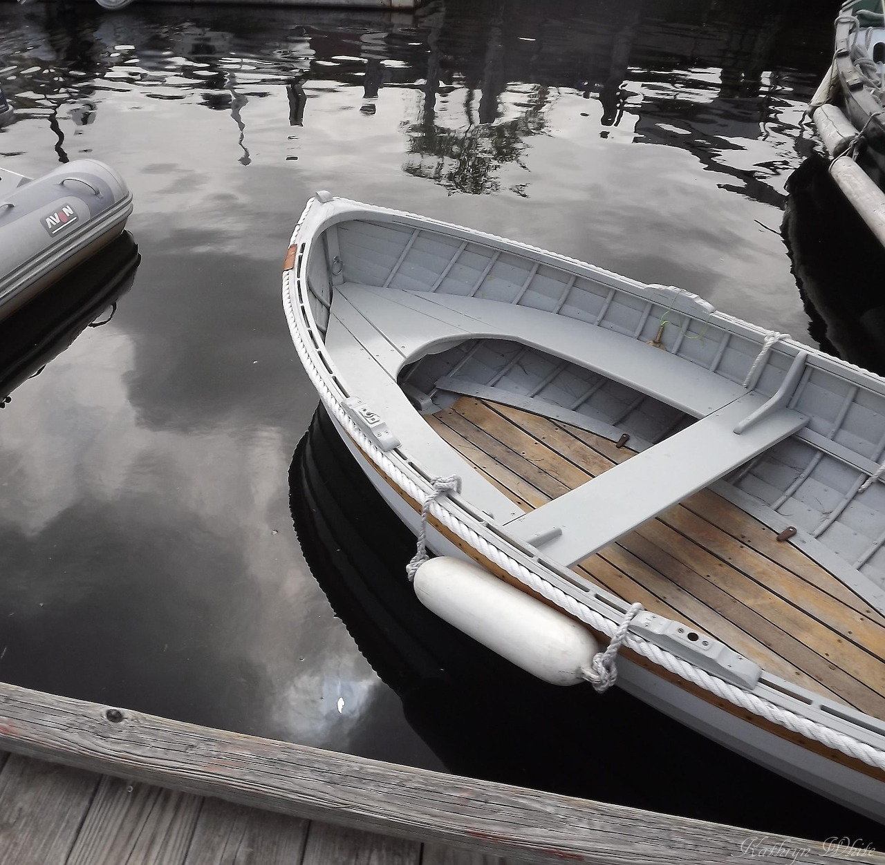 White dinghy tied beside a dock on calm reflective water