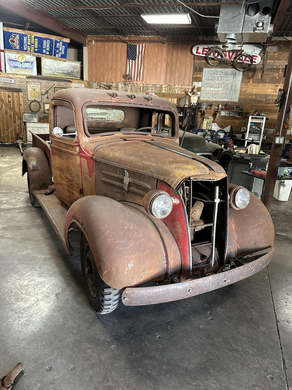 Rusty vintage 1930s pickup truck parked inside a garage with an American flag on the wall