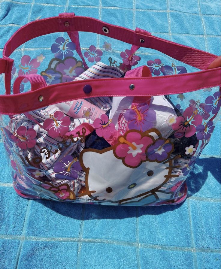Transparent Hello Kitty floral beach bag with pink handles on a turquoise towel