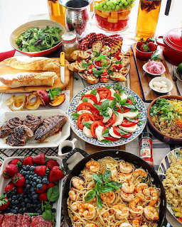 Overhead view of Italian food spread with pasta, caprese salad, meats, shrimp, bread, and drinks on wooden table