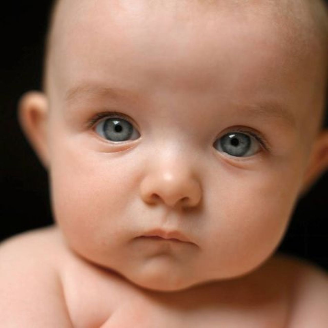 Close-up portrait of a blue-eyed baby looking at camera against dark background