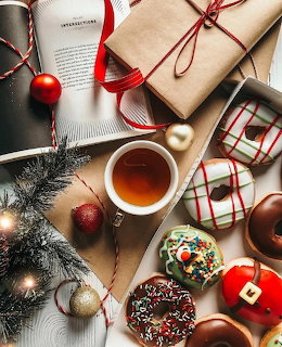 Overhead view of Christmas donuts, tea, gift boxes, ornaments, and evergreen branches on wood table