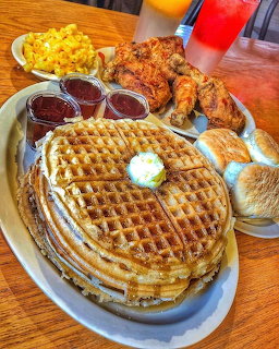 Plate of waffles with butter, fried chicken, sides of mac and cheese, coleslaw, and red drink on wooden table