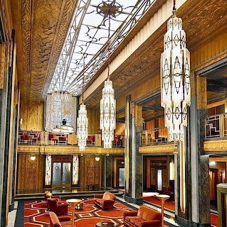 Art Deco lobby with marble columns, hanging chandeliers, geometric floor, and decorative glass ceiling