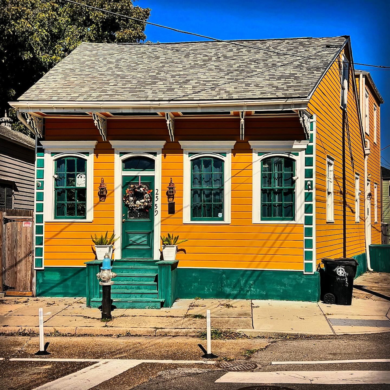 Colorful yellow and green shotgun-style house with white columns and green front steps under a blue sky