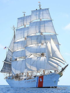US Coast Guard tall ship with full white sails on calm ocean under blue sky