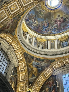 Looking up at an ornate church dome interior with colorful frescoes and gold decorations in Rome