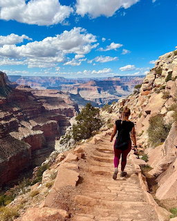 Person hiking down rocky trail with Grand Canyon vista and blue sky