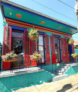 Colorful house with red shutters, turquoise porch, blue roof, and decorative flower baskets on a sunny street