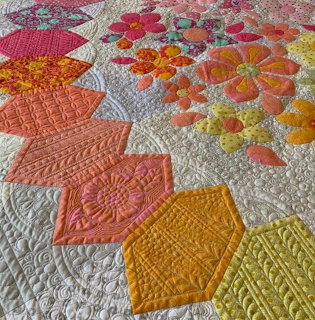 Colorful hexagonal quilt with coral, yellow, orange patches and floral designs on white fabric with decorative stitching