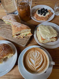 Cafe table with latte art, sandwich, pastry, and toast topped with cream and blueberries