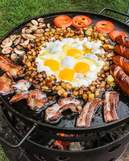 Skillet breakfast with eggs, bacon, sausage, potatoes, mushrooms, and tomatoes on an outdoor grill