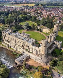 Aerial view of Warwick Castle with stone walls, towers, and surrounding green landscape