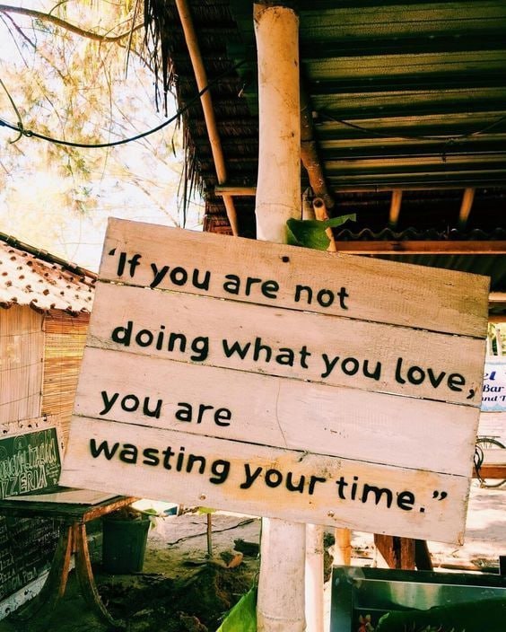 Rustic wooden sign with motivational quote about doing what you love, displayed outdoors under a shelter.