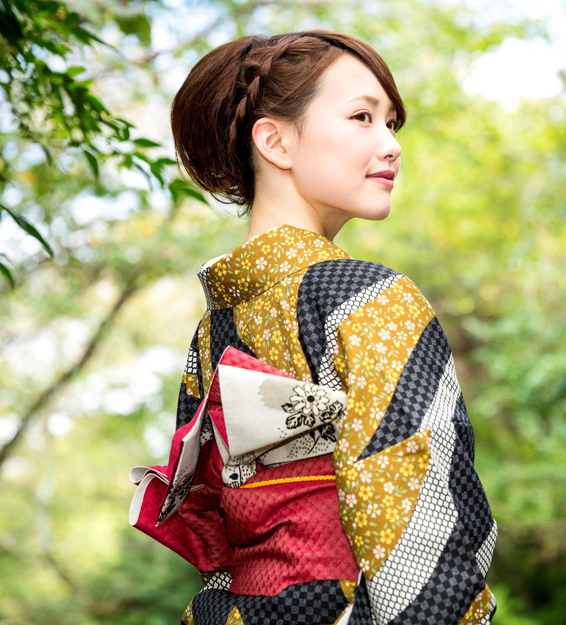 Woman in a patterned kimono standing outdoors with blurred green trees behind her