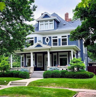 Blue Victorian house with white trim and front porch surrounded by green lawn and trees