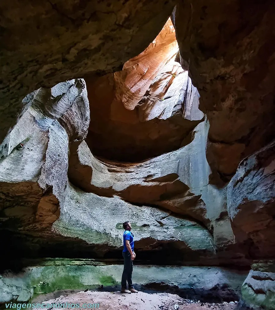 Person standing inside a sandstone cave beneath a skylight opening