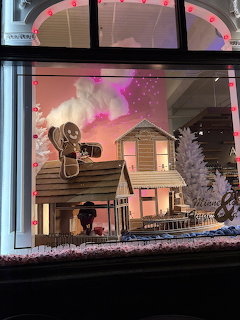 Christmas store window display with miniature houses, gingerbread man, white trees, and pink sky backdrop