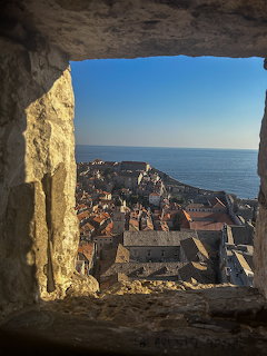 Historic stone window framing aerial view of Dubrovnik old town with red roofs and blue sea beyond