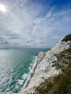 White chalk cliffs and sea stacks of The Needles extending into calm turquoise water under cloudy sky