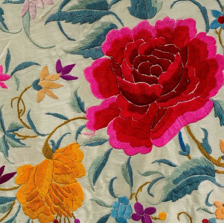 Close-up of a cream shawl embroidered with a large red flower, orange flower, and blue leafy vines