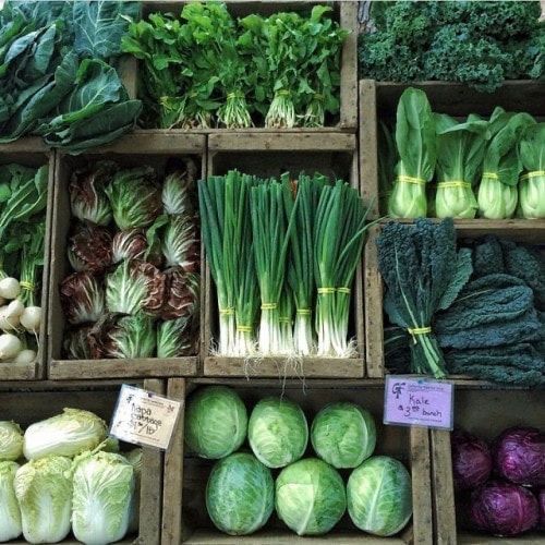 Assorted fresh green vegetables organized in wooden crates at a market display