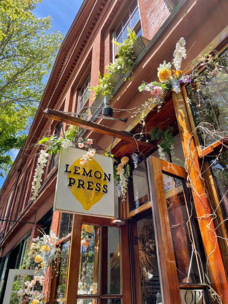 Lemon Press café sign with floral decorations on a brick and wood storefront on a sunny day