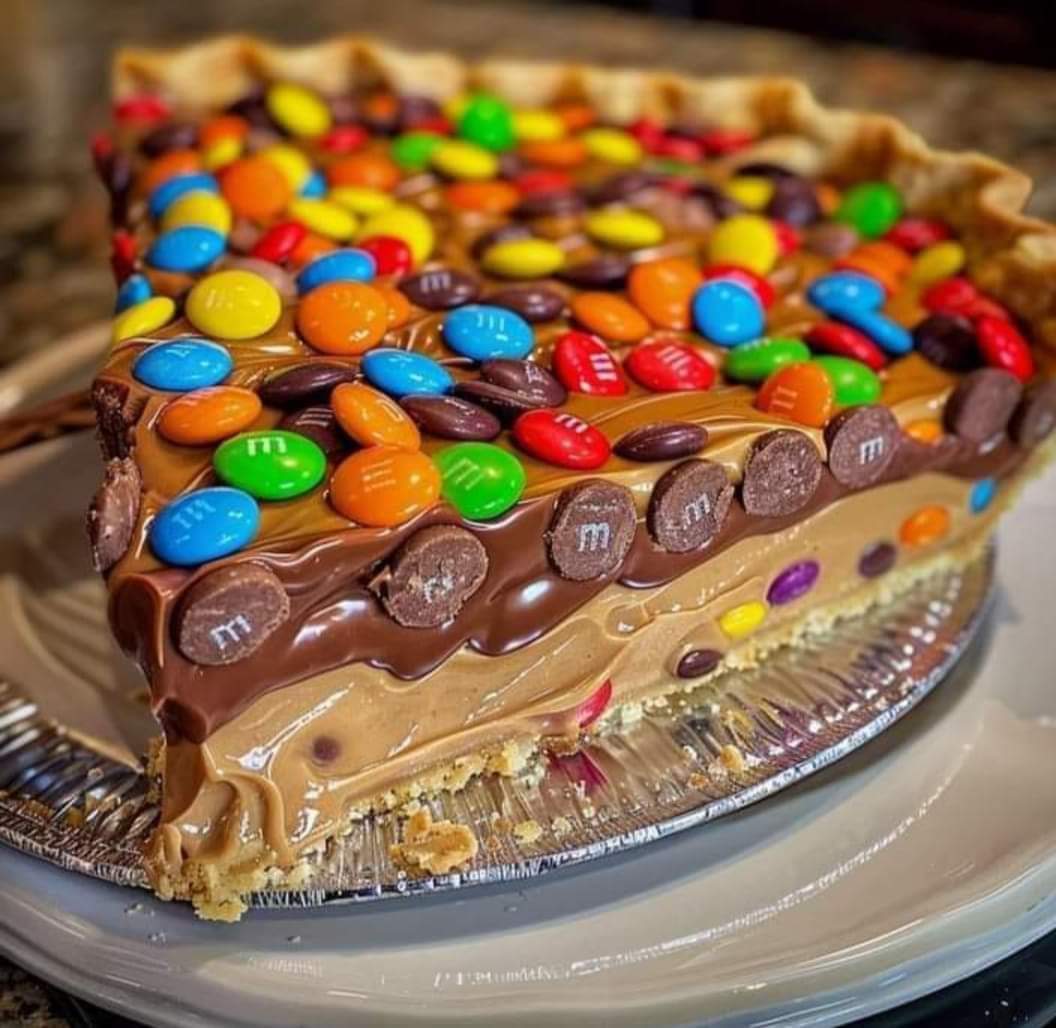 Multi-layer chocolate cake decorated with colorful candies and chocolate buttons on silver platter