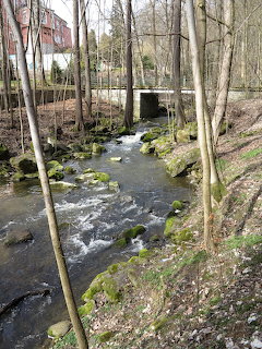 Rocky stream with mosy boulders flowing through a forest under a small bridge in early spring
