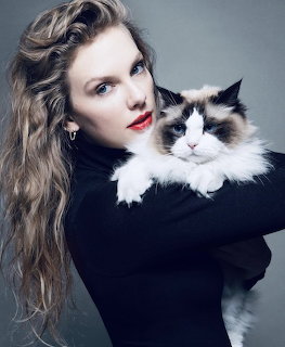 Woman with wavy blonde hair in black clothing holding a fluffy tuxedo cat in a studio portrait