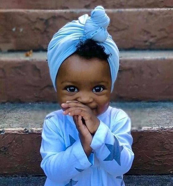 Young girl in blue headwrap with hands near face in shy pose