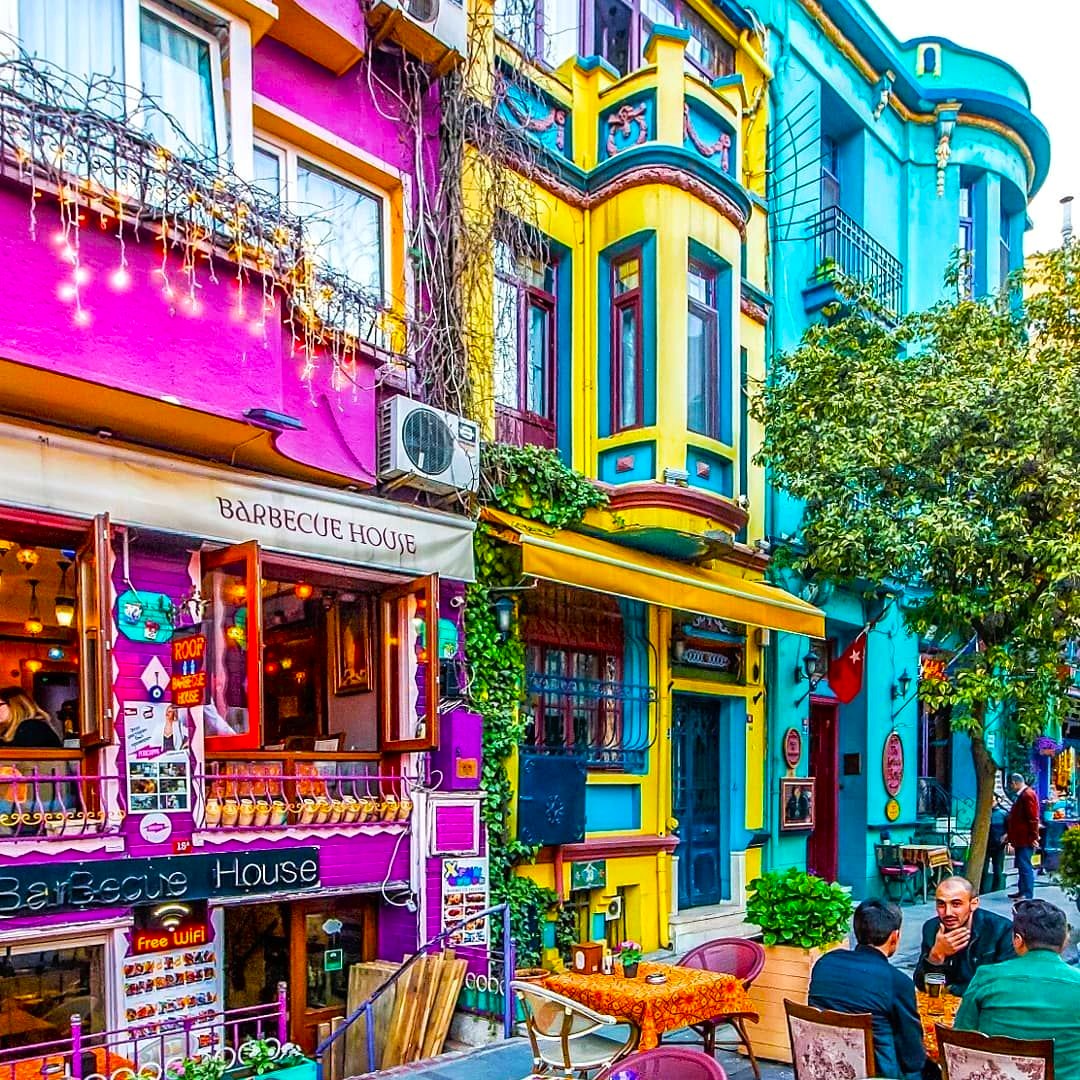 Colorful multi-story buildings with pink, yellow, and blue facades along a narrow Istanbul street with outdoor cafes