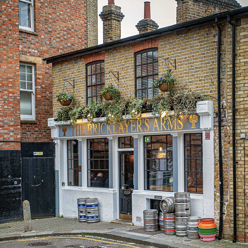 Bricklayers Arms pub in Putney with yellow brick facade, white storefront, hanging baskets, and beer kegs