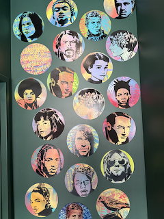 Colorful pop art style circular portraits of celebrities arranged on a dark green wall as street art