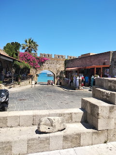 Medieval stone gate and courtyard in Rhodes old town with palm trees and fortification walls under clear blue sky