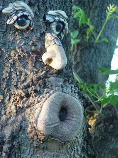Tree trunk with decorative face sculpture featuring bulging eyes, pointed nose, and round open mouth