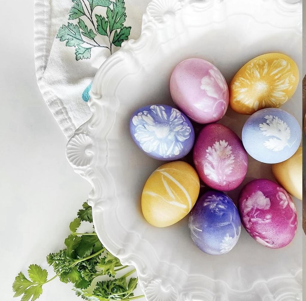 Colorful dyed Easter eggs with botanical leaf prints on a decorative white plate with herbs