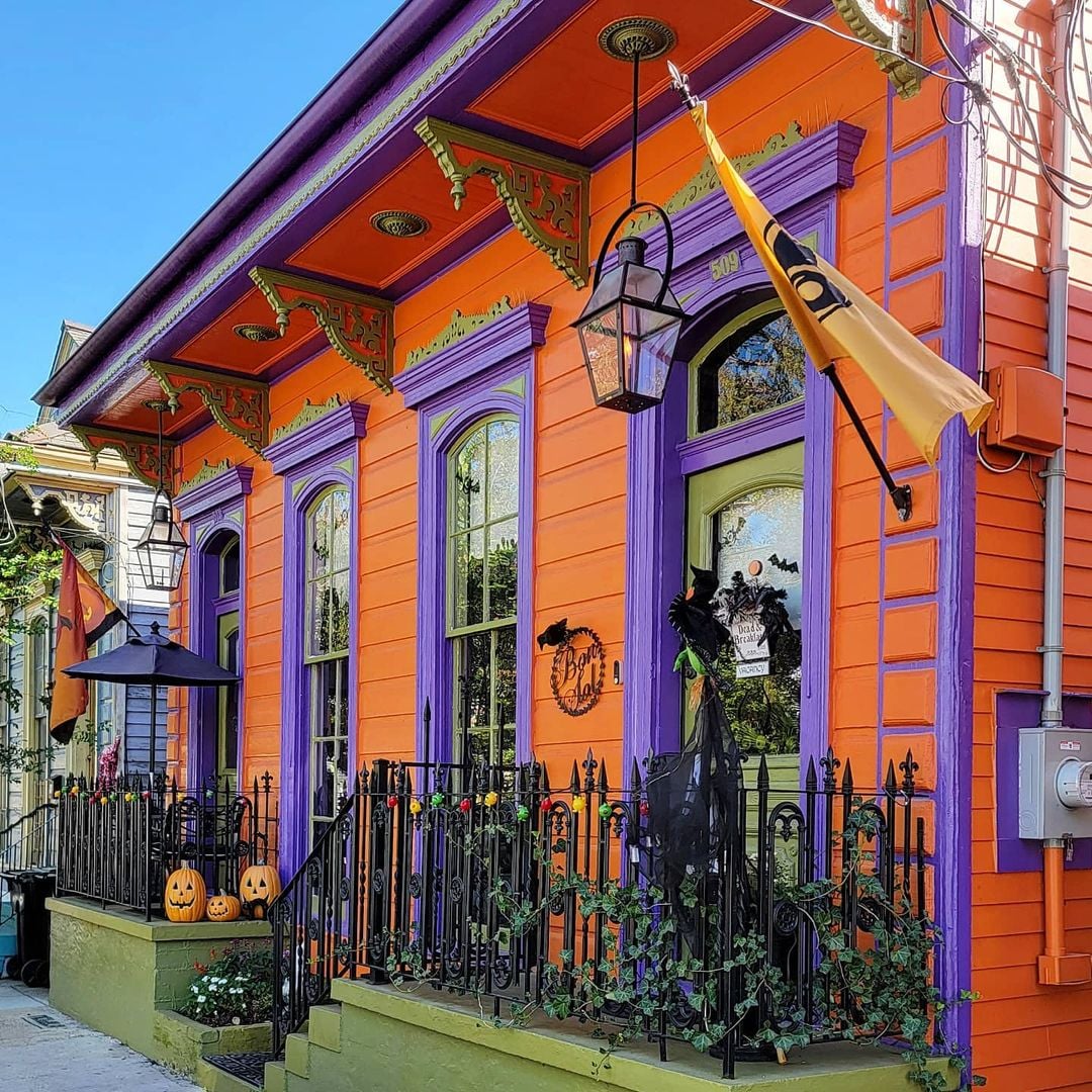 Bright orange Victorian house with purple accents and Halloween decorations including pumpkins and wreath on front porch