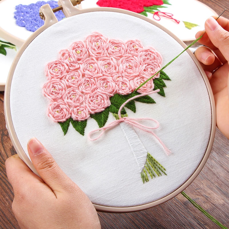 Hands holding an embroidery hoop with pink rose bouquet embroidery on white fabric