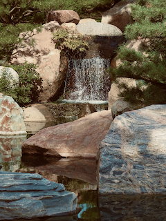 Small waterfall over rocks into a calm pond in a Japanese garden