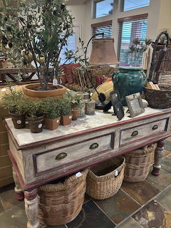Rustic wooden console table with poted herbs, green elephant lamp, wicker baskets, and garden accessories