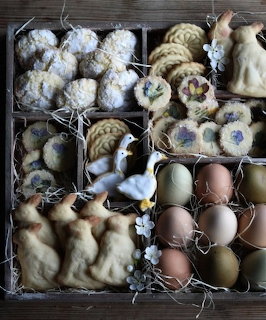 Wooden compartment box filled with Easter cookies, decorated eggs, and spring treats arranged with straw