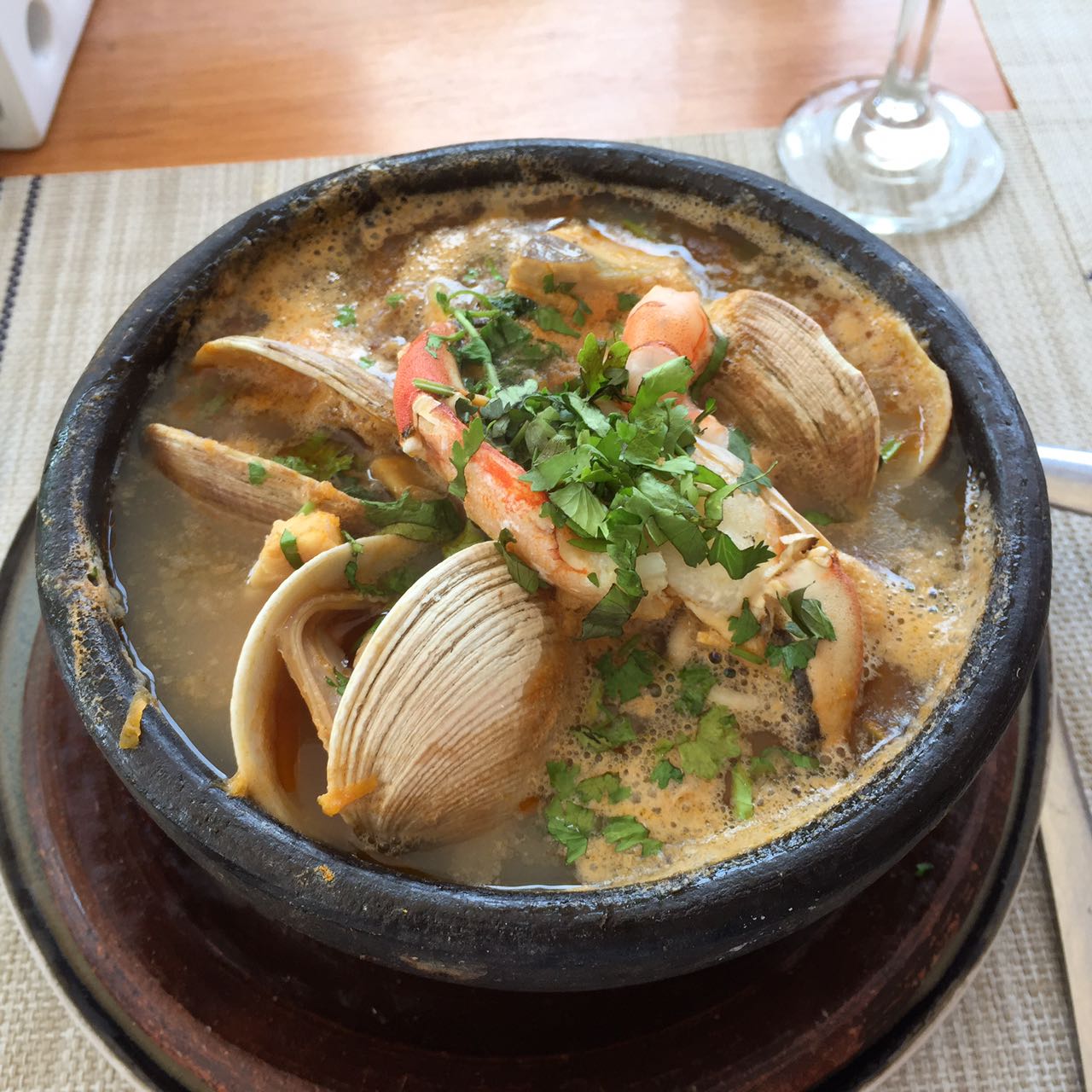 Black bowl of mariscal seafood stew with clams, shrimp, broth, and chopped herbs